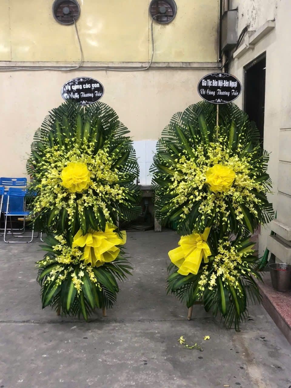 Đôi vòng hoa lan vàng dáng đứng đặt trước phòng lễ, băng chữ ghi tên người viếng