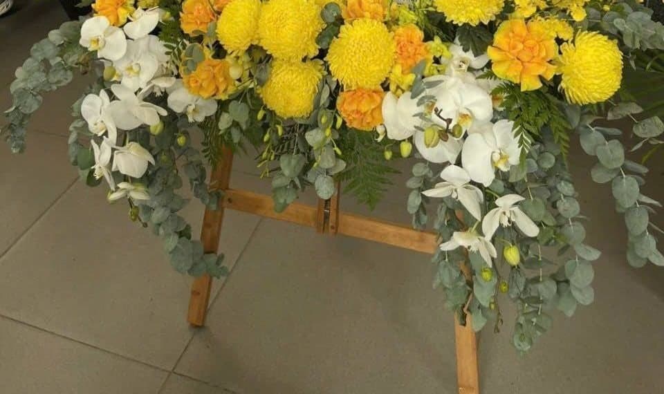 Kệ hoa gỗ kết cúc vàng và lan trắng dùng đặt bảng cáo phó ở nhà tang lễ
