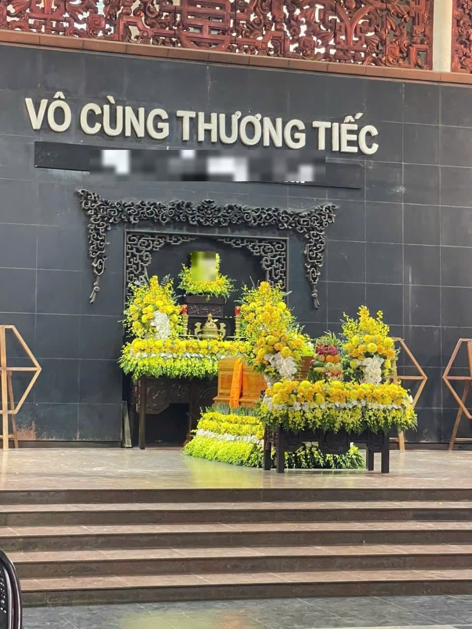 Chữ nổi gắn trên tường đá phía trên hương án phủ hoa cúc vàng trong nhà tang lễ