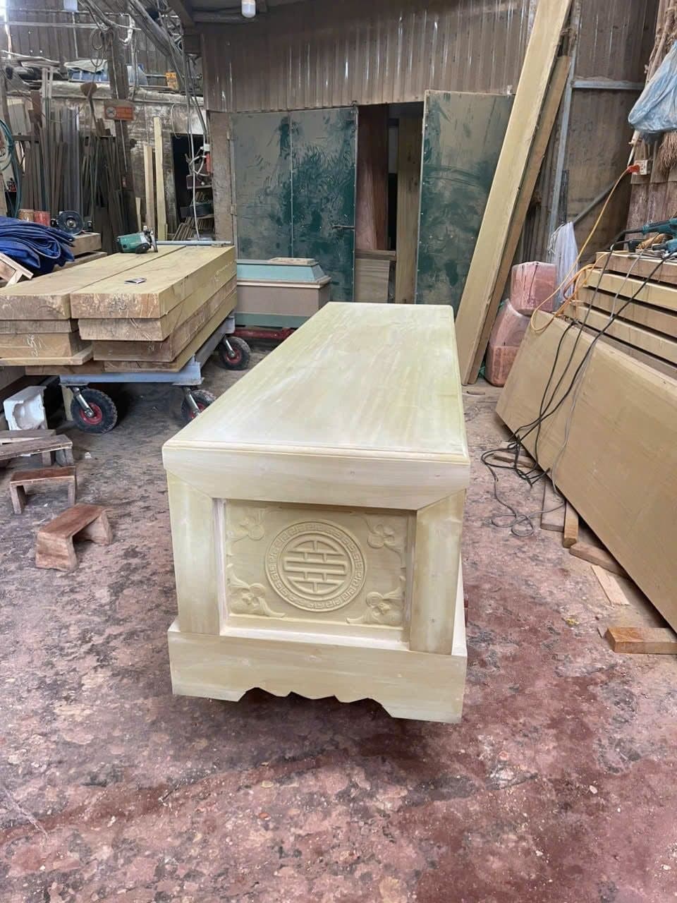 Quan tài gỗ vàng tâm hoàn thiện mộc đặt giữa xưởng, xung quanh là ván gỗ xẻ xếp thành chồng