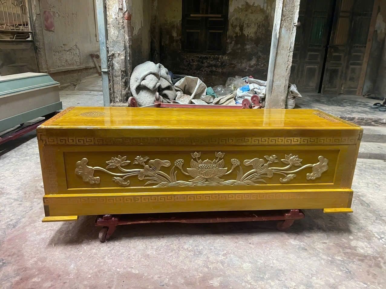 Thân quan tài gỗ vàng tâm sơn cánh gián chạm nổi hoa sen và dây lá, viền hồi văn quanh chân